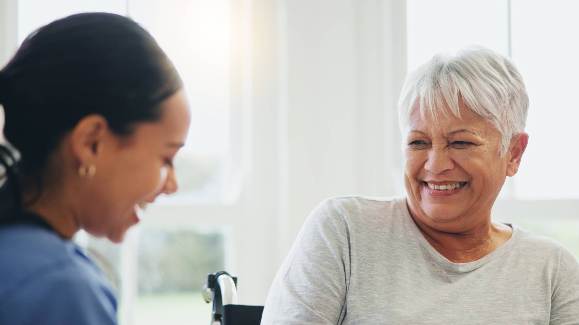 A senior woman and her nurse laughing together.